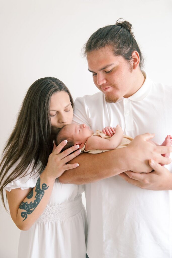 family with newborn and mom kissing newborn in a photography studio