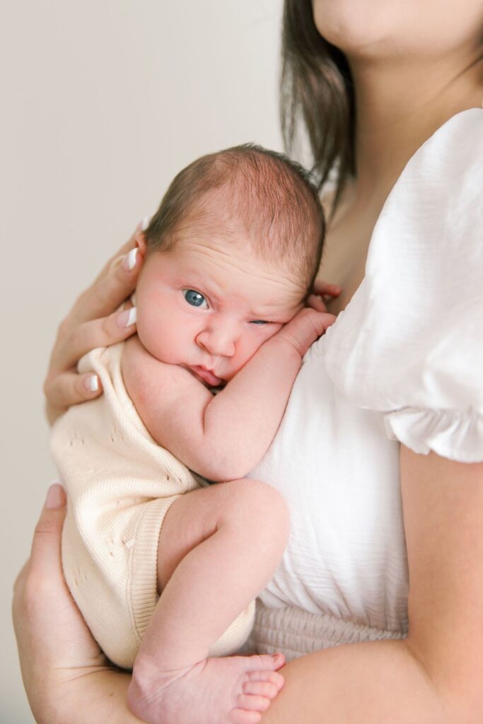 close up of newborn baby with eye open held by mom