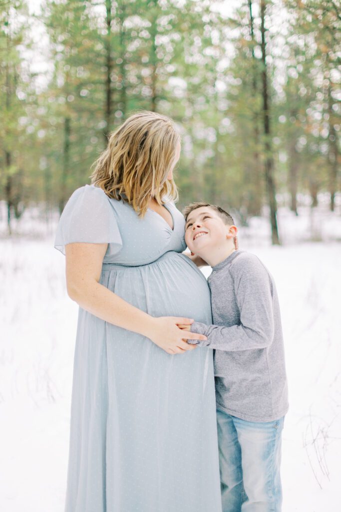 expecting mom and her son embracing for family photos in the winter